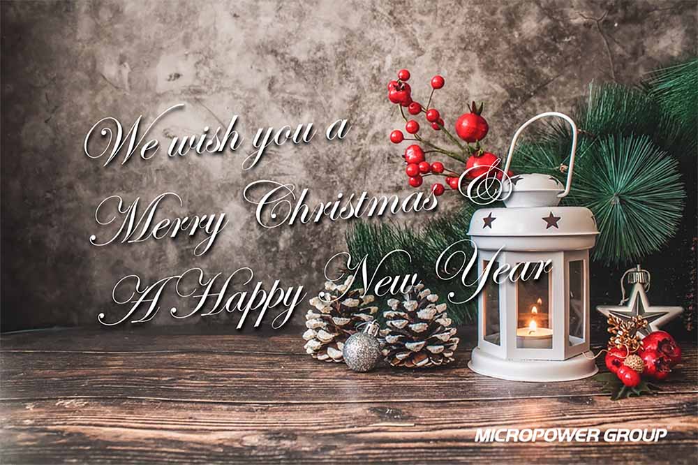 Christmas card from Micropower Group with a white lantern with a lit candle, cones and red berries.